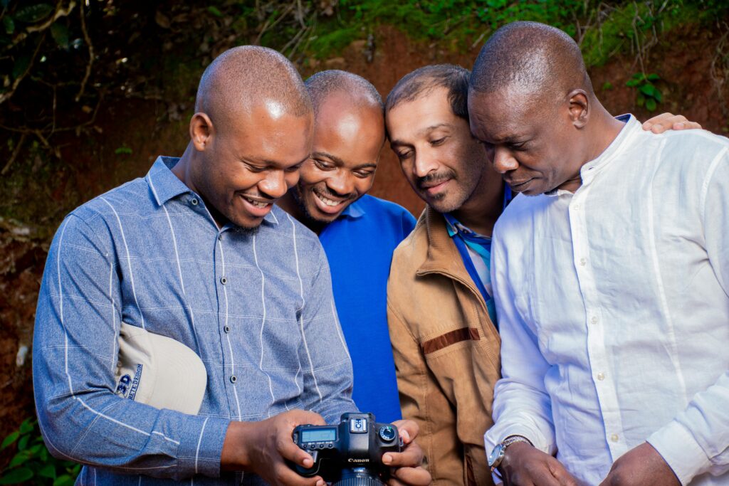 A group of four smiling African men happily review photos on a camera in Tanzania.